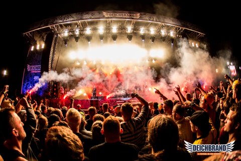Die Hauptbühne auf dem Deichbrand Festival am späten Abend. Die Broilers singen auf der Bühne und eine große Publikumsmenge feiert davor. 